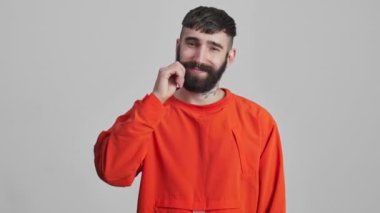 Genç, yakışıklı, pozitif esmer adam gri duvar arkasında sakalına dokunuyor..