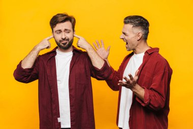 30 'lu yaşlarda, kırmızı tişörtlü iki yakışıklı adamın sarı arka planda yalıtılmış bir şekilde kavga ederken görüntüsü.