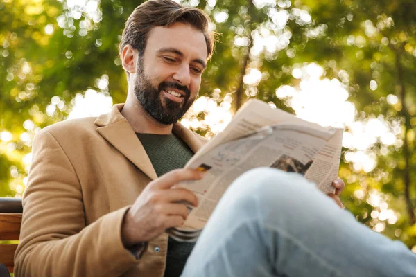 Kép Jóképű Felnőtt Férfi Kabátban Mosolyog Újságot Olvas Miközben Padon — Stock Fotó