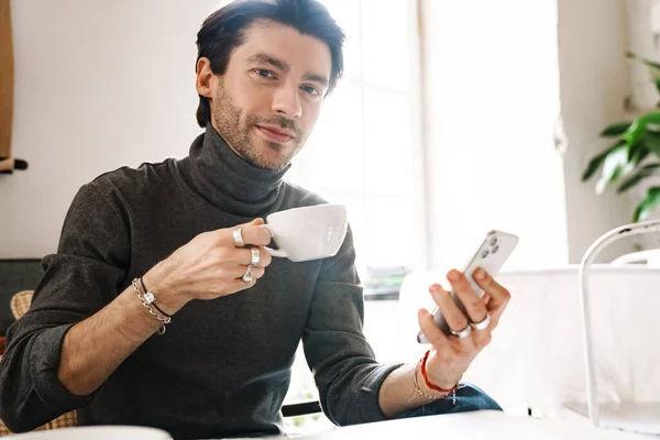 카페에서 테이블에 커피를 마시고 핸드폰을 사용하는 잘생긴 코카서스 젊은이의 — 스톡 사진
