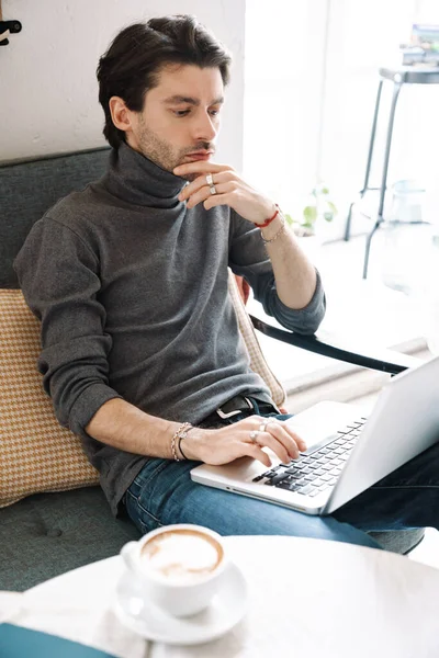 ハンサムな白人青年のイメージラップトップコンピュータで作業し 現代のカフェでコーヒーを飲む — ストック写真