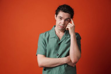 Kafası karışmış beyaz adamın görüntüsü kırmızı arka planda izole edilmiş kamerada poz verip düşünüyor.