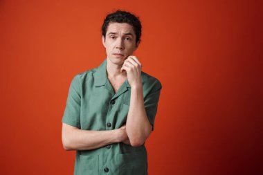 Kafası karışmış beyaz adamın görüntüsü kırmızı arka planda izole edilmiş kameraya bakıyor ve poz veriyor