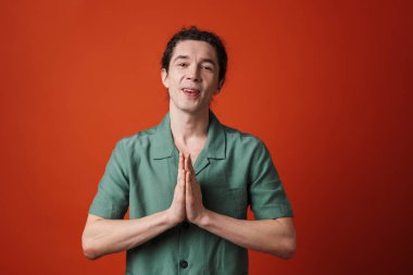 Portakal rengi arka planda avuçlarıyla kamerada poz veren mutlu yakışıklı bir adam.