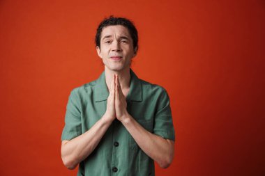 Portakal rengi arka planda avuçlarıyla kamerada poz veren genç yakışıklı bir adam.