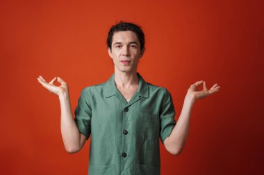 Kamerada poz veren ve turuncu arka planda zen hareketi yapan yakışıklı bir genç resmi.