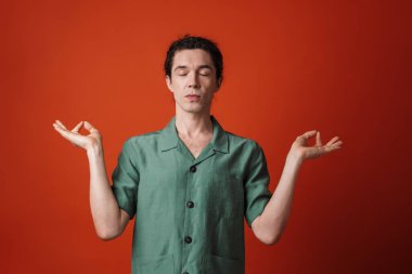 Kamerada poz veren ve turuncu arkaplanda zen hareketi yapan sakin yakışıklı bir adam görüntüsü.