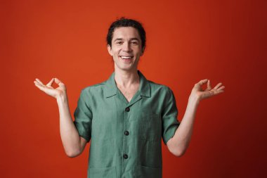 Gülümseyen ve turuncu arka planda Zen hareketi yapan neşeli yakışıklı bir adam görüntüsü.