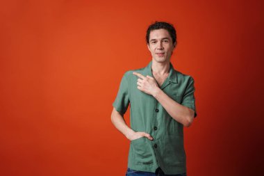 Mutlu ve mutlu bir adamın portakal rengi arka planda izole edilmiş bir şekilde gülümsemesi ve işaret etmesi.