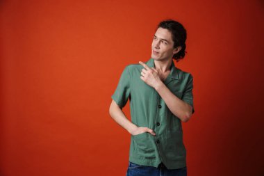 Mutlu ve mutlu bir adamın portakal rengi arka planda izole edilmiş bir şekilde gülümsemesi ve işaret etmesi.