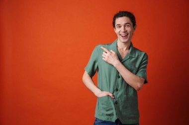 Gülen ve parmakla işaret eden neşeli yakışıklı bir adam portakal rengi arka planda izole edilmiş.
