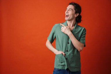 Gülen ve parmakla işaret eden neşeli yakışıklı bir adam portakal rengi arka planda izole edilmiş.