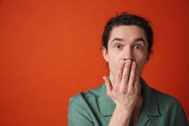 Turuncu arka planda izole edilmiş kameraya şok veren genç bir adamın görüntüsü.