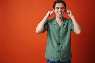 Turuncu arka planda gülen ve kulaklarını tıkayan mutlu yakışıklı bir adam görüntüsü.