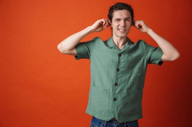 Kameraya bakıp kulaklarını turuncu arka plana tıkayan mutsuz yakışıklı adam görüntüsü.