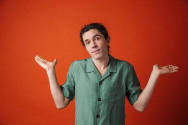 Kafası karışmış yakışıklı bir adamın portakal rengi arka planda elleri havada poz vermesi.