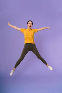 Neşeli, heyecanlı, genç, güzel bir bayan sporcunun uzunluğu menekşe arka planında izole bir şekilde duruyor, atlıyor.