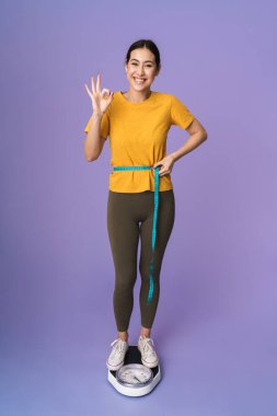 Menekşe arkaplan üzerinde izole edilmiş, belinde bant tutan neşeli, genç ve güzel bir sporcunun boyu, tamam mı?