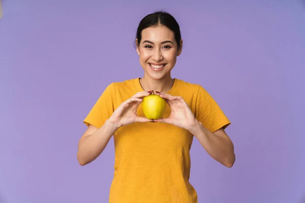 年轻而快乐的漂亮女运动员被紫色的背景隔离着 露出黄色的苹果 — 图库照片