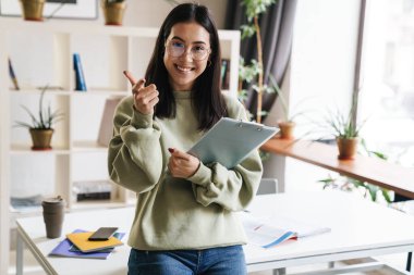 Oldukça sevimli, mutlu, neşeli, genç bir kızın elinde seni işaret eden bir not panosu var..