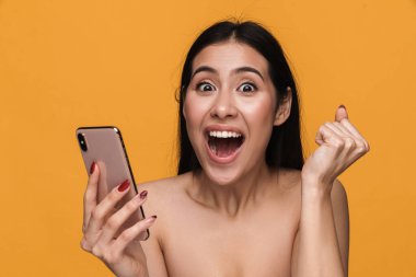 Sarı arka planda cep telefonu tutarken gülümseyen, yarı çıplak, beyaz esmer bir kadının güzel portresi.