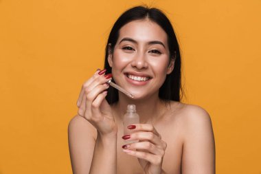 Beyaz tenli, yarı çıplak bir kadının güzel portresi gülümseyen ve elinde sarı arka planda izole edilmiş yüz kremi şişesi tutan.