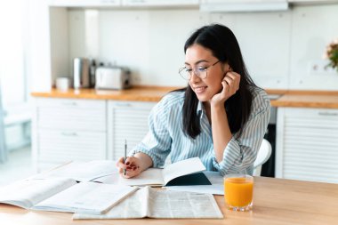 Mutfakta, evde oturup notlar yazan, mutlu ve konsantre olmuş genç bir kadının görüntüsü..
