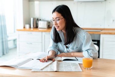 Evde mutfaktaki konsantre olmuş esmer bir kadının evde ders çalışırken notlar yazması..