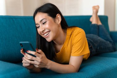 Evdeki kanepede cep telefonuyla gülümseyen güzel bir esmer kadının fotoğrafı..