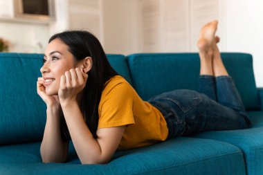 Evdeki kanepede oturan oldukça iyimser, esmer bir kadının fotoğrafı..