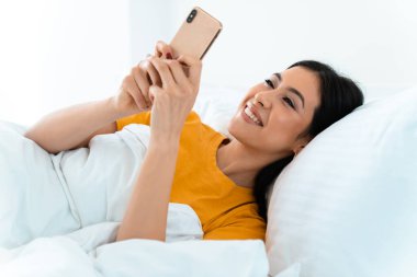 Güzel, gülümseyen bir genç kadının görüntüsü. Evde, evde cep telefonu kullanarak yatakta yatıyor..