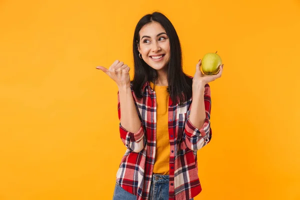 一个微笑的高加索女人把大拇指放在一边 把苹果夹在黄色的背景上 — 图库照片