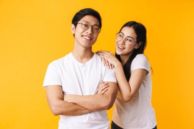 Sarı arka planda tek başına duran, günlük kıyafetler giyen güzel, neşeli, genç Asyalı bir çiftin portresi.