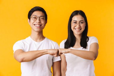 Sarı arka planda izole edilmiş, yumruk tokuştururken günlük kıyafetler giyen güzel, neşeli, genç Asyalı bir çiftin portresi.