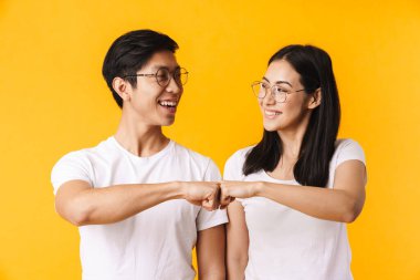 Sarı arka planda izole edilmiş, yumruk tokuştururken günlük kıyafetler giyen güzel, neşeli, genç Asyalı bir çiftin portresi.