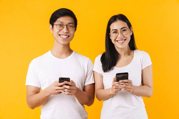 一对年轻貌美的亚洲年轻夫妇穿着休闲装站在黄色背景下 使用手机的肖像 — 图库照片
