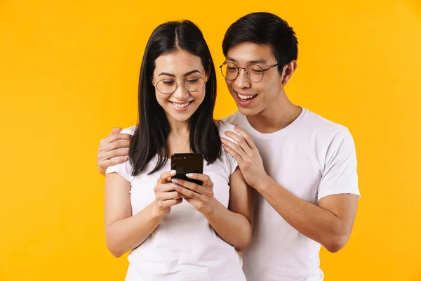 一对年轻貌美 快乐的亚洲年轻夫妇穿着休闲装 孤零零地站在黄色背景下 使用手机的画像 — 图库照片