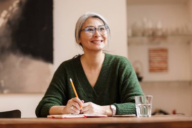 Muhteşem, olgun, güzel, kır saçlı, kapalı alanda notlar yazan bir kadının görüntüsü..