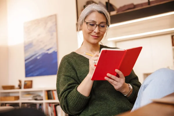 Photo Pleased Mature Woman Eyeglasses Making Notes Diary While Sitting — Stock Photo, Image