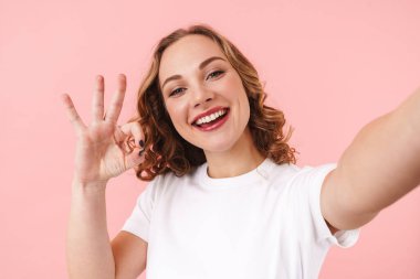 Pembe duvar arkasında izole edilmiş şirin, mutlu, genç bir kadının fotoğrafı. Kamerayla bir selfie çek..