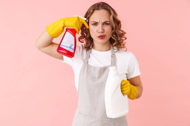 Ciddi bir genç kadın resmi, eldivenli, pembe duvar arkasında izole edilmiş, elinde temizleyici sprey ve şişeyle intihar silahı jesti yapıyor..