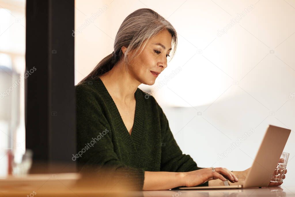 Image of a mature amazing positive optimistic woman indoors using laptop computer.