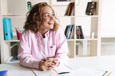 Ev ödevi yaparken ve odada otururken gözlük takan neşeli bir kadının fotoğrafı.