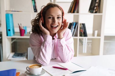 Odada ödev yaparken kablosuz kulaklık takan güzel bir kadının gülümseme fotoğrafı.