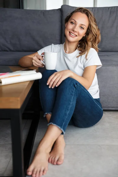 티셔츠를 커피를 마시며 거실에 매력적 여성의 — 스톡 사진