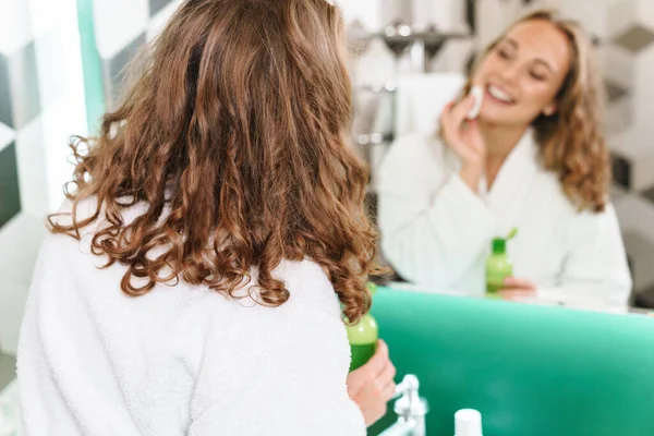 Sorridente Giovane Donna Bionda Che Indossa Accappatoio Applicare Lozione Viso — Foto Stock