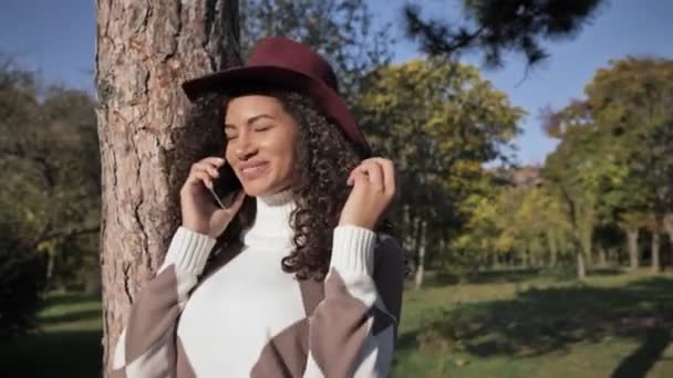 若いですCheery正アフリカの女の子で帽子歩く屋外で緑の自然公園で話しています携帯電話 — ストック動画