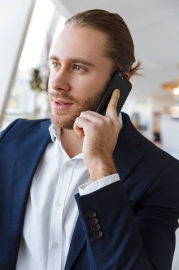 Ofiste cep telefonuyla konuşan yakışıklı genç bir işadamının görüntüsü.