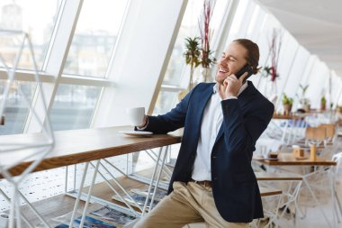 Ofiste cep telefonuyla konuşan yakışıklı, gülen genç bir işadamının resmi..