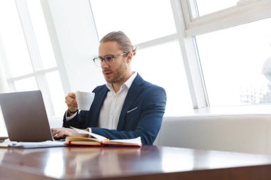 Ofiste dizüstü bilgisayarla çalışan yakışıklı, ciddi konsantre genç bir iş adamının resmi..